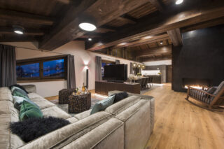 Sofas facing fireplace and flat-screen TV with dining area and kitchen at Nidus Penthouse in Lech