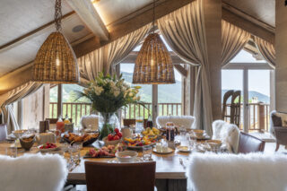 Dining table set for breakfast with mountain views through French doors opening to balcony at Chalet la Loze in Méribel