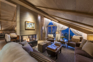 Living space with island fireplace separating lounge and dining areas at Chalet la Loze in Méribel