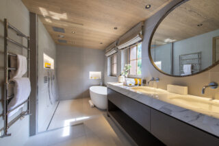 Master bedroom en suite bathroom with oval bath tub, twin rain showers and twin sinks at Chalet la Loze in Méribel