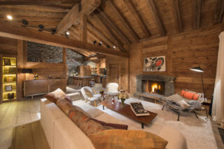 Lounge area with open fireplace and view through to kitchen kitchen in the evening at Chalet Bibi in Verbier