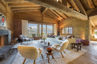 Sofa and armchairs arranged around fireplace with French doors opening to balcony at Chalet Bibi in Verbier