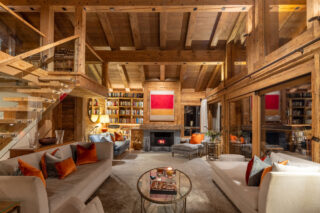 Living room with open fireplace and stairs up to mezzanine at Chalet les Étrennes in Verbier
