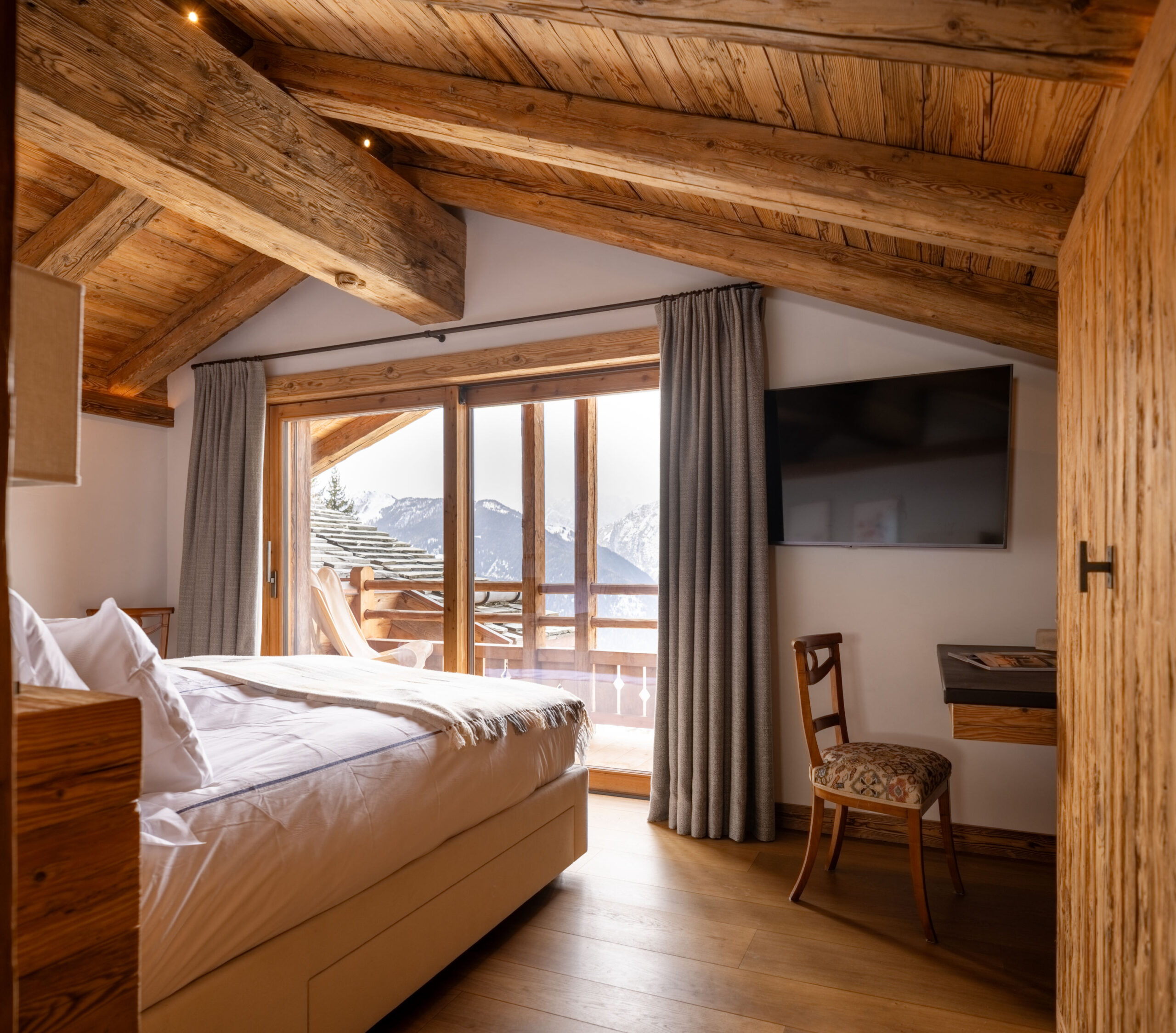 Master bedroom with TV, desk and French windows opening to private balcony at Chalet Pierrier in Verbier