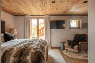 Master bedroom with TV, armchair and doors to terrace at Chalet Sirocco in Verbier