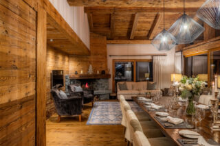 Night time view of open plan living and dining area with corner fireplace at Chalet Sirocco in Verbier