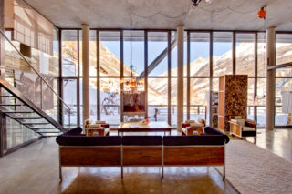 View from the rear of the living space with the sun on snow-covered mountains seen through the floor to ceiling windows at the Heinz Julen Loft in Zermatt
