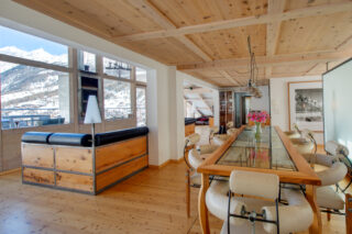 Dining area with glass-topped table next to the living area at the Heinz Julen Penthouse in Zermatt