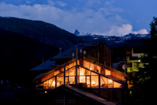 Exterior view at dusk of the Heinz Julen Penthouse in Zermatt with interior lights in the living space