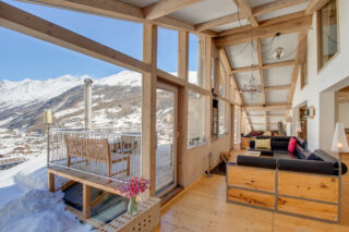 Living space with double height windows and balcony outside Custom build leather and wood sofas in the living space at the Heinz Julen Penthouse in Zermatt